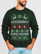 A man wearing a dark green Christmas crewneck sweatshirt with a festive knit pattern featuring reindeer, snowflakes, and the text 'YOUR EXCEL SKILLS ARE TRASH' in white and green.