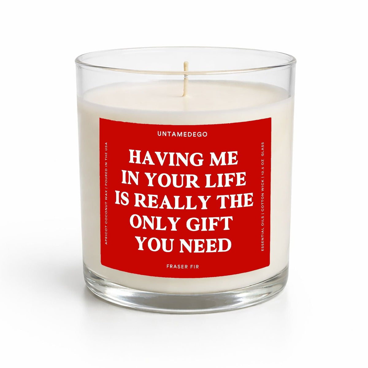 A white wax candle in a clear glass jar with a red front label that reads, 'HAVING ME IN YOUR LIFE IS REALLY THE ONLY GIFT YOU NEED' and the brand name UNTAMEDOO at the top.