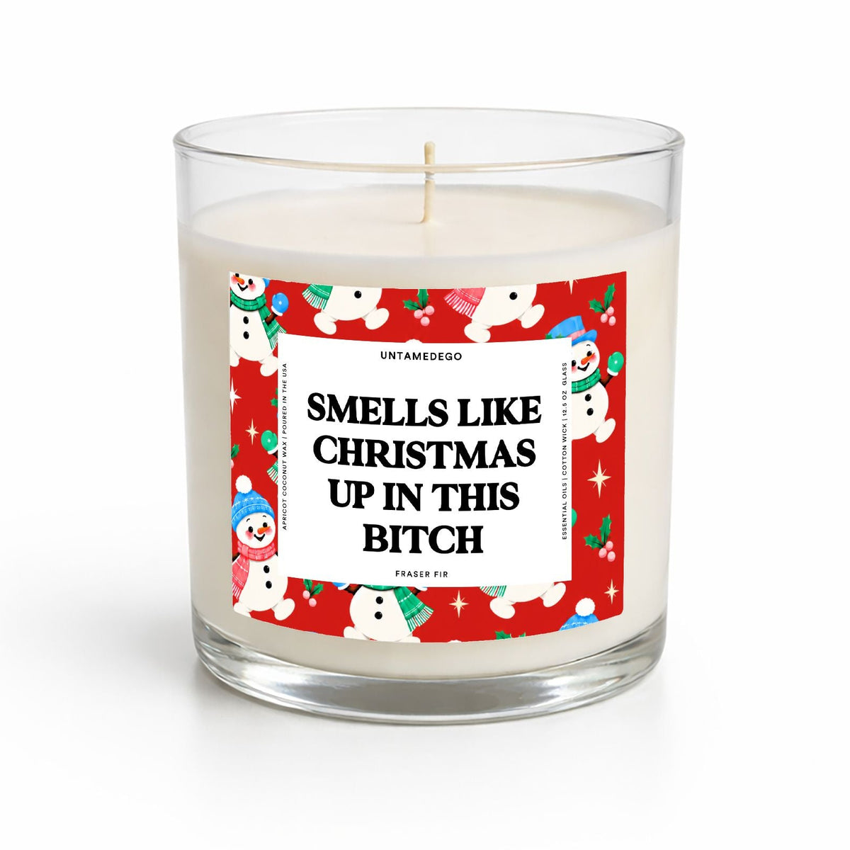A clear glass jar candle with white wax and a festive red label featuring snowman illustrations and the text 'SMELLS LIKE CHRISTMAS UP IN THIS BITCH'.