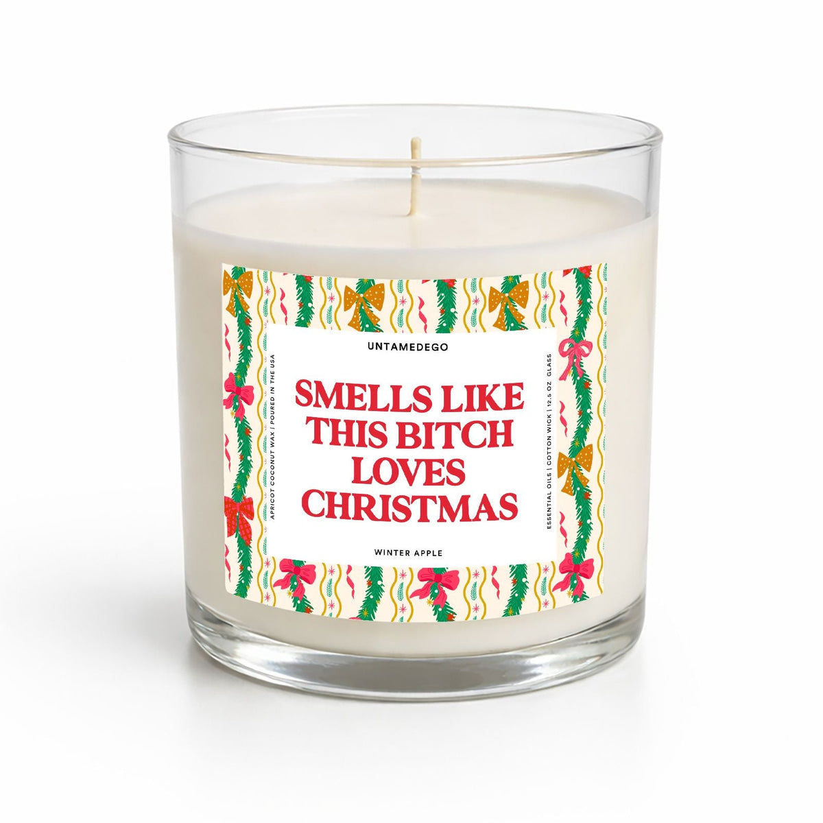 A clear glass jar candle with white wax and a humorous Christmas-themed label that reads 'SMELLS LIKE THIS BITCH LOVES CHRISTMAS' in red text, surrounded by green holly and red bows, on a white background.