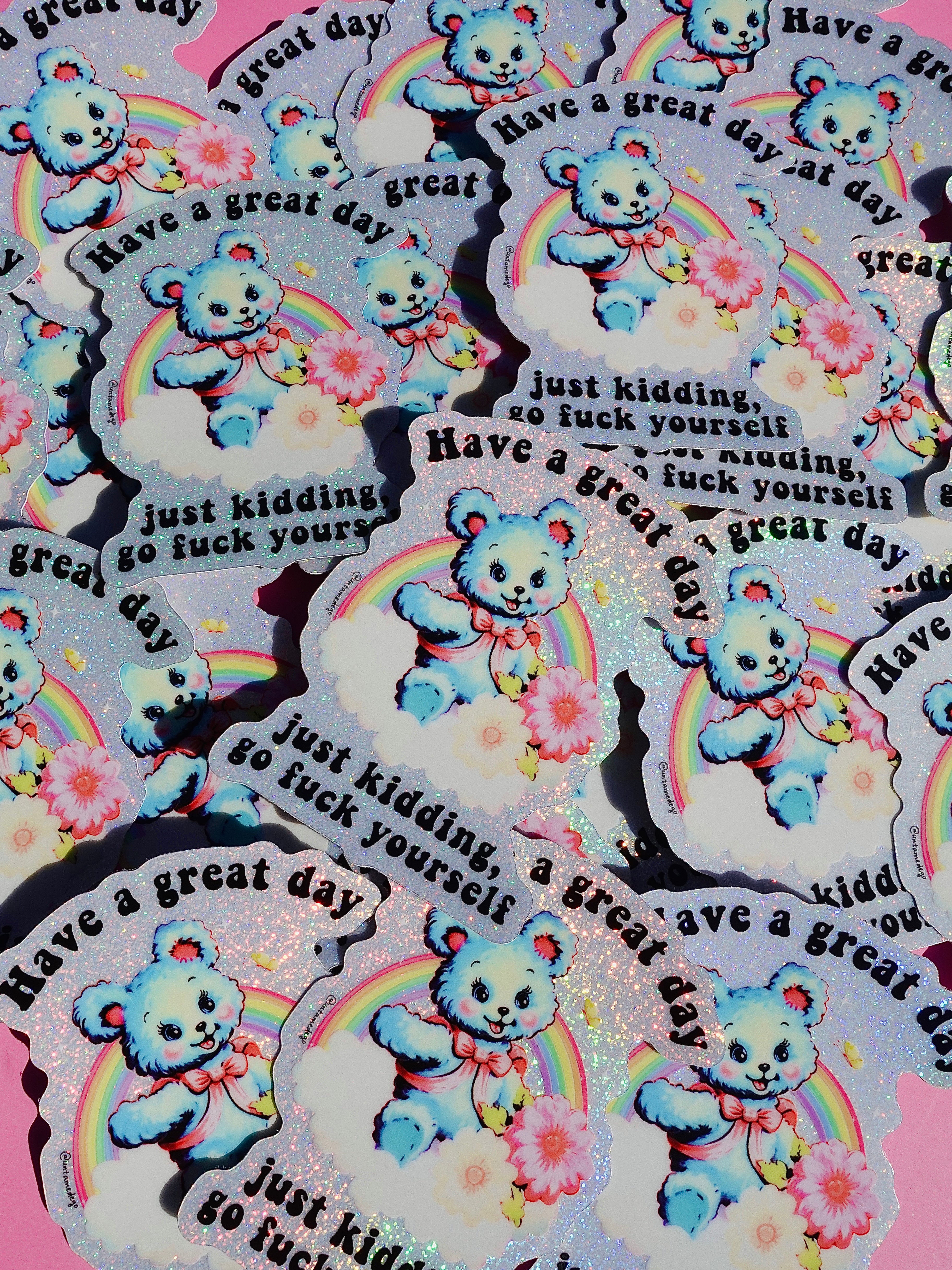 Funny holographic vinyl sticker with pastel blue bear, rainbow, and flowers. Text reads “Have a great day, just kidding, go f*ck yourself.”
