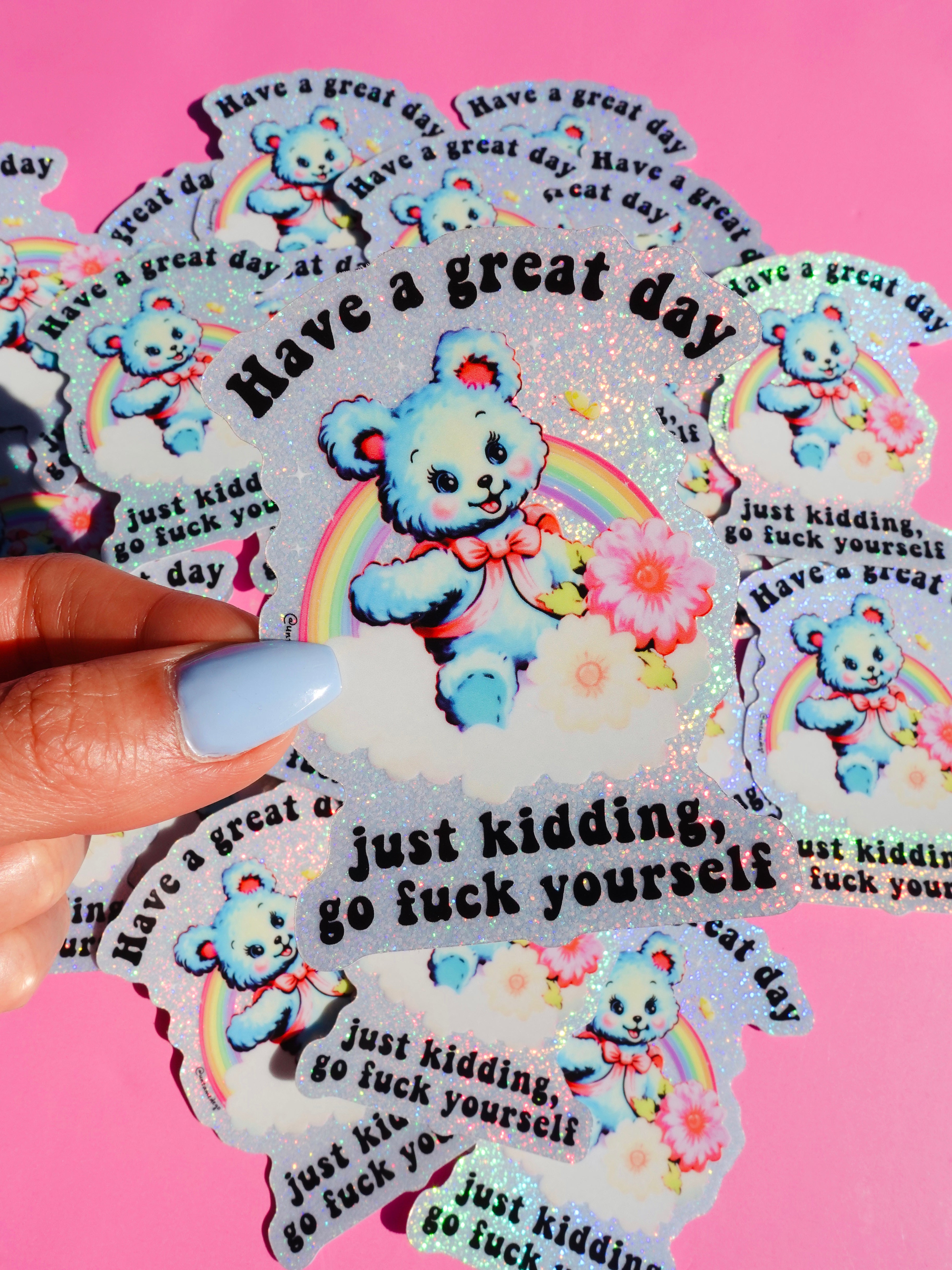 Funny holographic vinyl sticker with pastel blue bear, rainbow, and flowers. Text reads “Have a great day, just kidding, go f*ck yourself