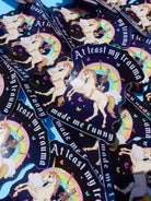 Holographic glitter vinyl stickers showing a skeleton riding a unicorn under a rainbow with butterflies and clouds. Bold white text reads At Least My Trauma Made Me Funny.