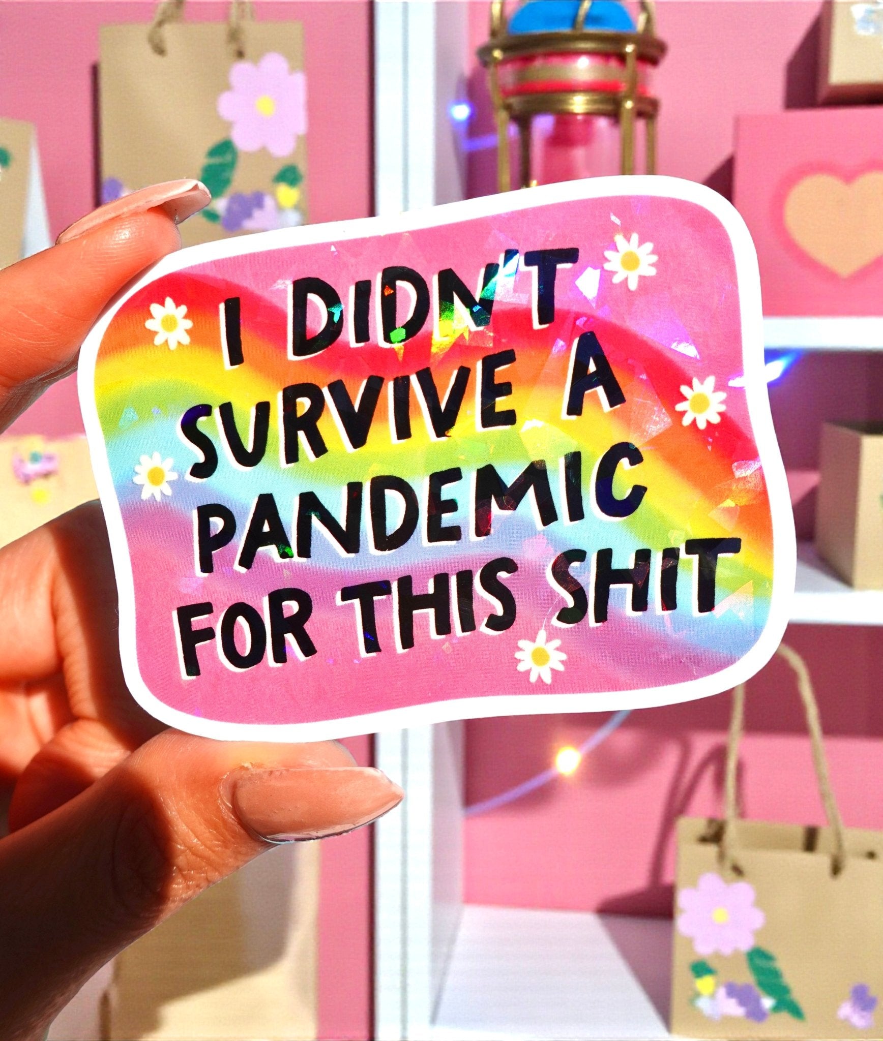 Rounded rectangle die-cut holographic vinyl sticker with a rainbow swirl background and white daisy accents along the border. Bold black text reads I Didn't Survive a Pandemic for This Shit.
