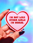 Heart-shaped sticker with text held by a hand against a colorful background