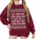 A woman wearing an oversized maroon crewneck sweatshirt with a white and green Christmas-themed graphic that reads, 'LAST CHRISTMAS I SAID I WOULD QUIT BUT THE VERY NEXT DAY I CAME INTO WORK.'.
