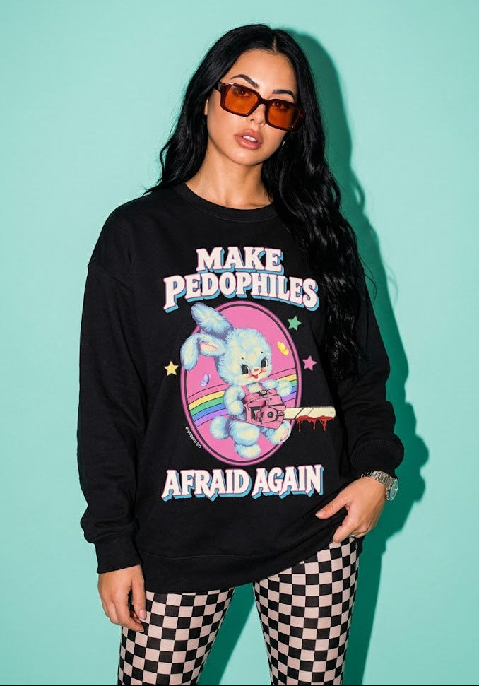 A woman modeling a black crewneck sweatshirt with a colorful graphic of a cartoon bunny and the text 'MAKE PEDOPHILES AFRAID AGAIN', paired with black and white checkered pants, set against a solid mint green background.