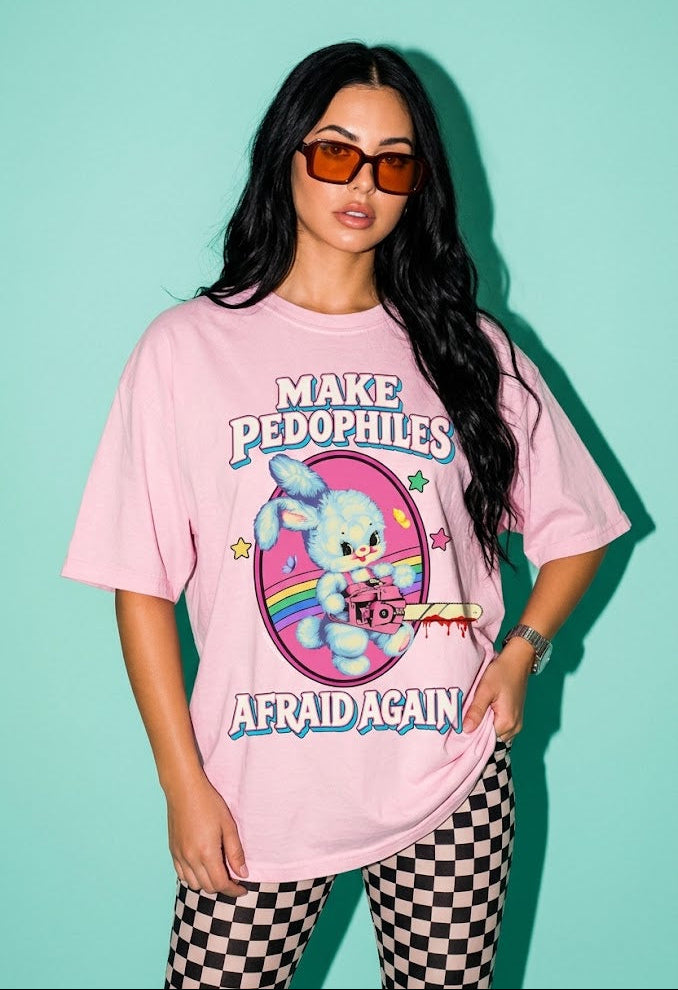 A woman modeling an oversized light pink graphic t-shirt with the text 'MAKE PEDOPHILES AFRAID AGAIN' and a cartoon bunny illustration, paired with black and white checkered pants against a mint green background.