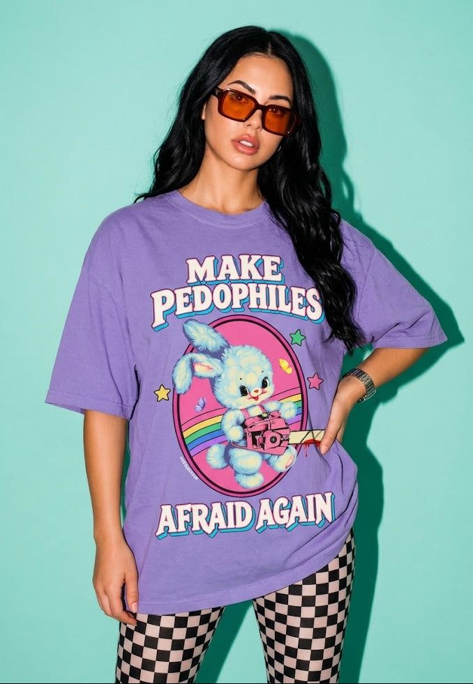A woman modeling an oversized lavender graphic t-shirt with the text 'MAKE PEDOPHILES AFRAID AGAIN' and a cartoon bunny illustration, paired with black and white checkered pants, against a solid mint green background.