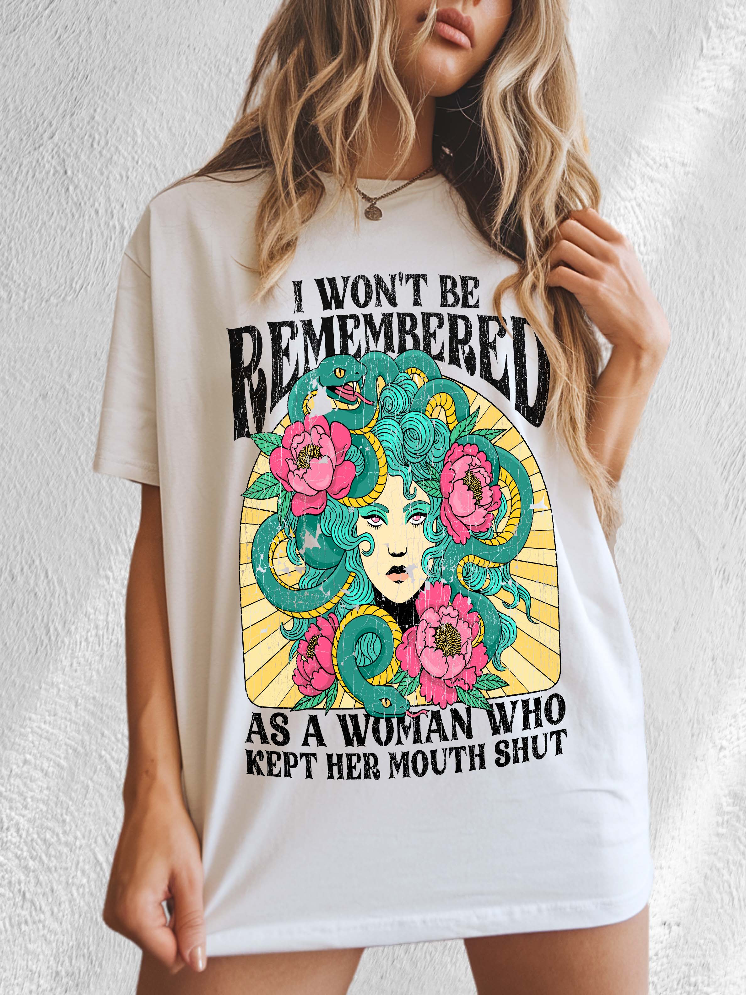 A woman modeling a white crew neck t-shirt with a graphic print in the center that reads 'I Won't Be Remembered As A Woman Who Kept Her Mouth Shut' surrounded by floral designs.