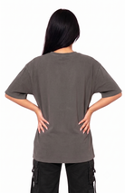 A woman viewed from the back wearing an oversized short-sleeve t-shirt in a washed dark gray color, paired with black cargo pants, against a plain white background.