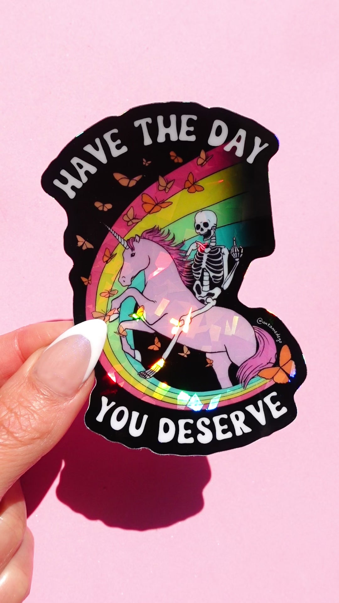 Funny holographic sticker with skeleton riding a unicorn and text “have the day you deserve” cute dark humor vinyl sticker