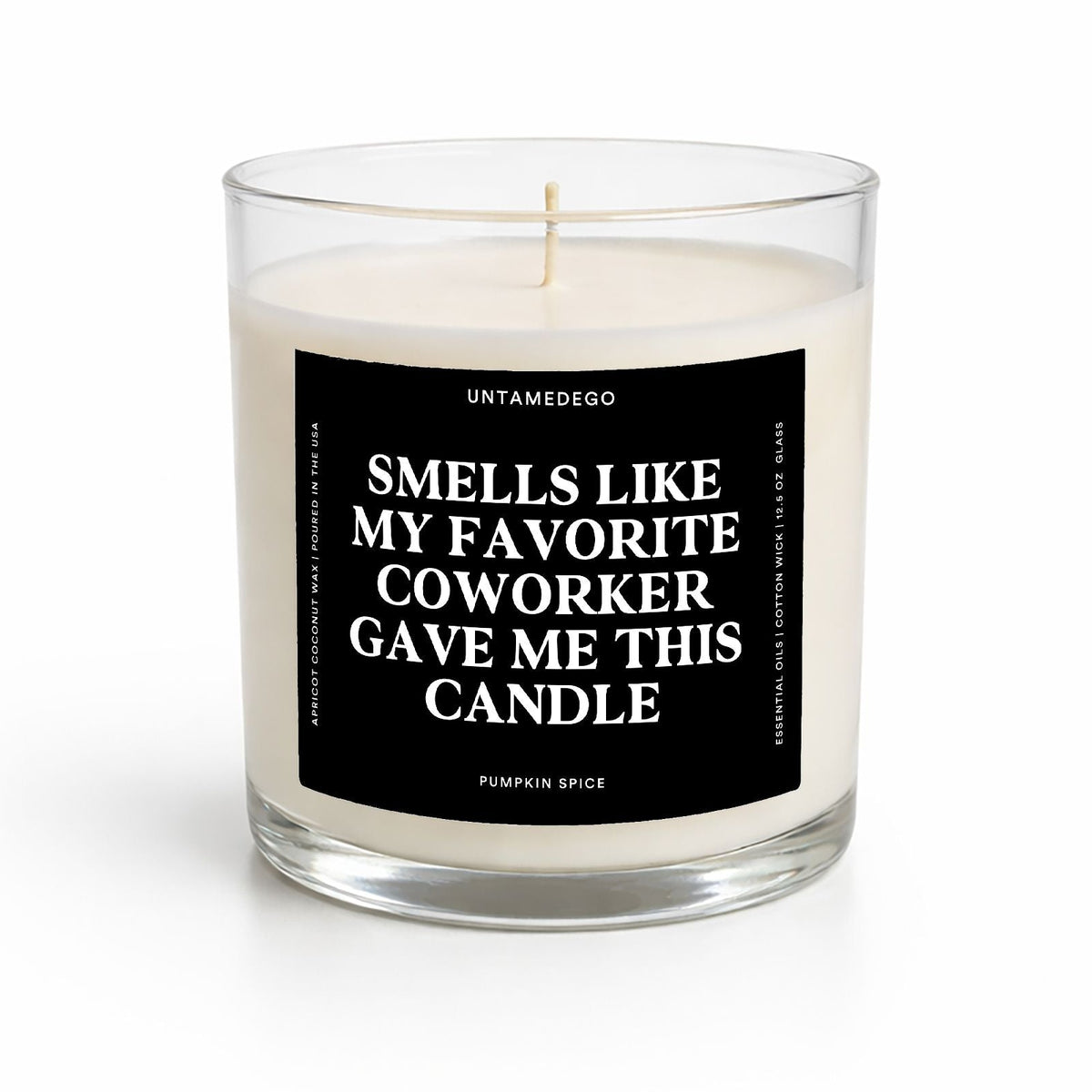 A single-wick candle in a clear glass jar with cream-colored wax and a black label featuring white text that reads, 'SMELLS LIKE MY FAVORITE COWORKER GAVE ME THIS CANDLE' and 'PUMPKIN SPICE' at the bottom. The brand 'UNTAMEDEGO' is visible at the top of the label.