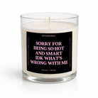 A sea salt + orchid scented candle in a clear glass jar with a black label featuring pink text that reads 'SORRY FOR BEING SO HOT AND SMART IDK WHAT'S WRONG WITH ME' by Untamedeo.