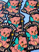 Holographic glitter protest sticker reading "Sugar Spice and Fuck ICE" held by a hand with painted nails, surrounded by multiple copies of the same sticker scattered on a dark surface.
