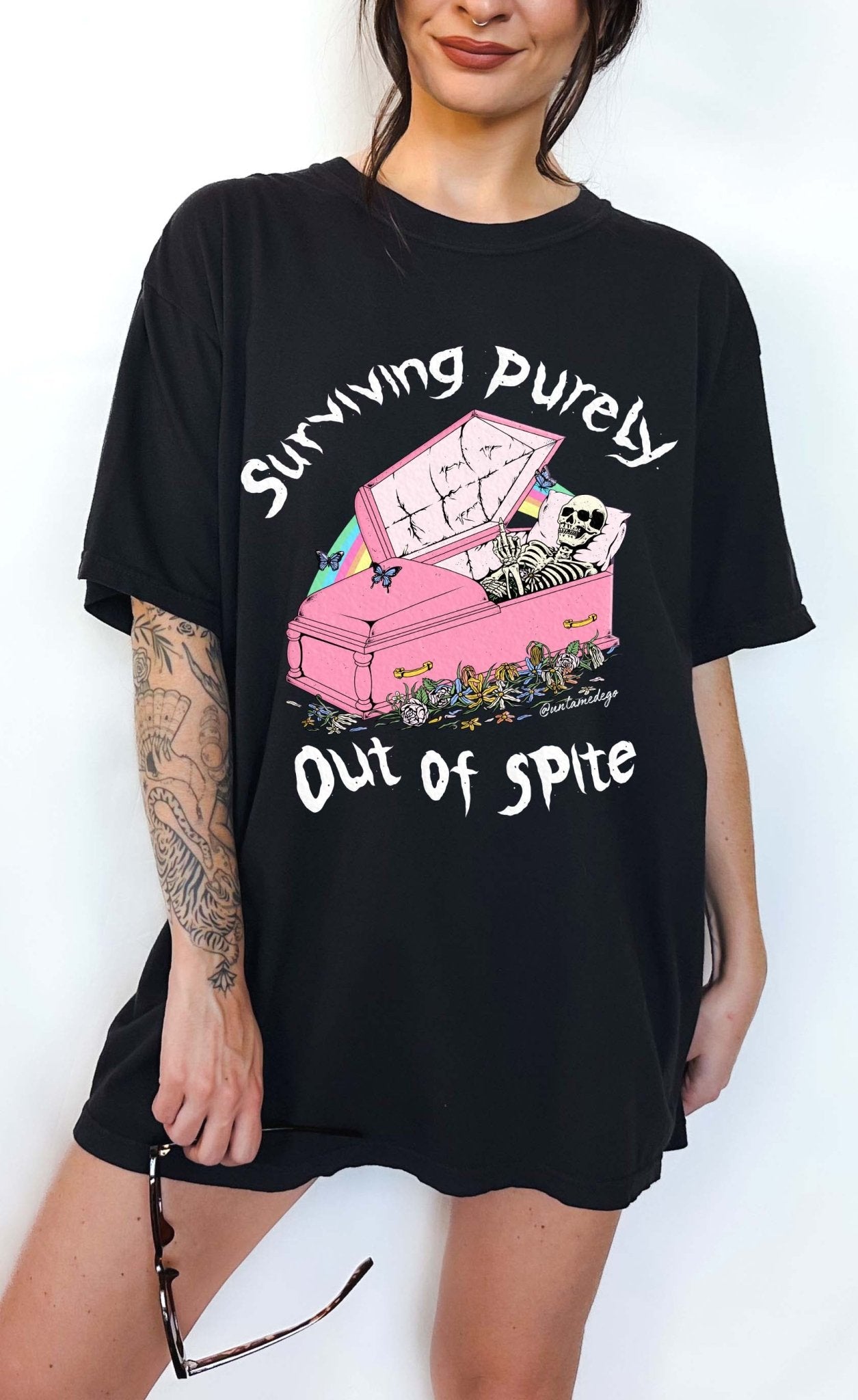 Funny graphic t-shirt with skeleton in coffin and text saying surviving purely out of spite