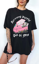 Funny graphic t-shirt with skeleton in coffin and text saying surviving purely out of spite