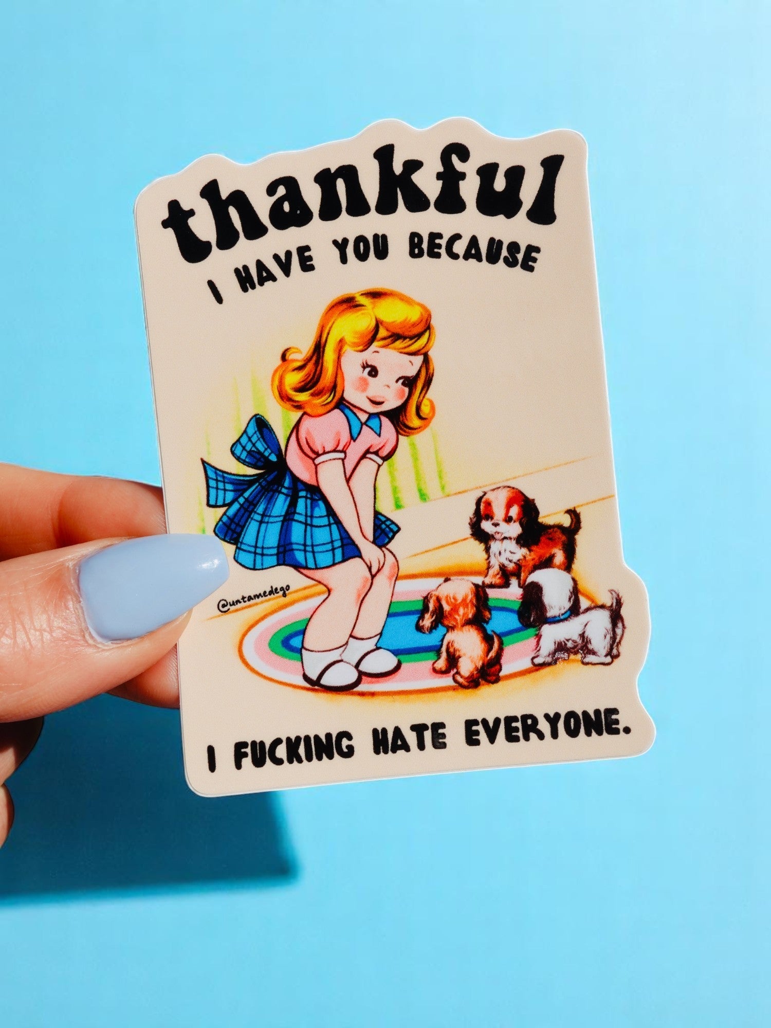 Die-cut glossy vinyl sticker featuring a retro-style illustration of a blonde girl in a blue dress sitting on a rug with two puppies. Text reads: Thankful I Have You Because I Fucking Hate Everyone.