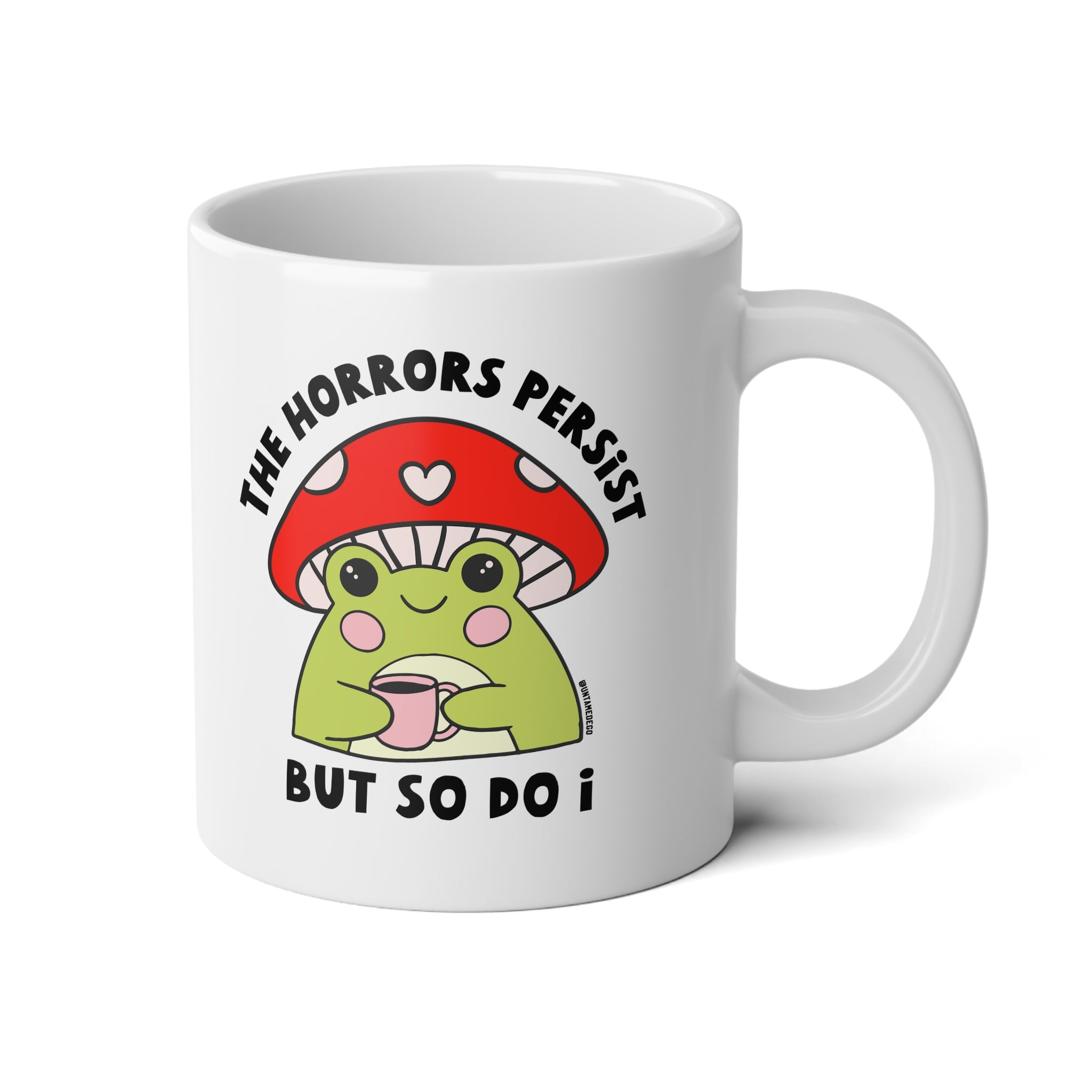 A white ceramic mug featuring a cute cartoon graphic of a green frog wearing a red mushroom cap and holding a pink mug, with the text 'THE HORRORS PERSIST BUT SO DO I' printed in black.