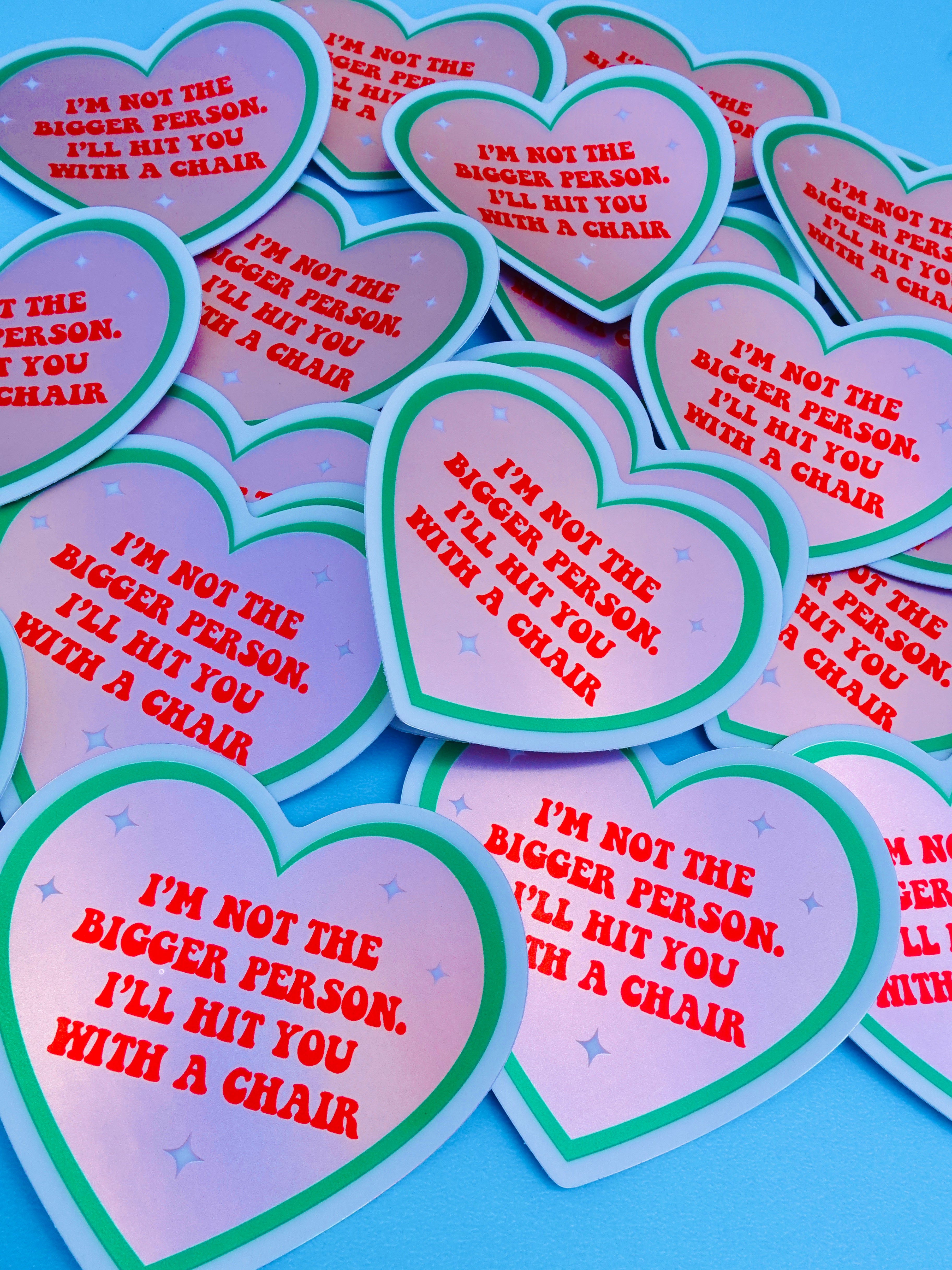 Funny heart-shaped vinyl sticker with pink and green border. Text reads “I’m Not the Bigger Person. I’ll Hit You with a Chair.