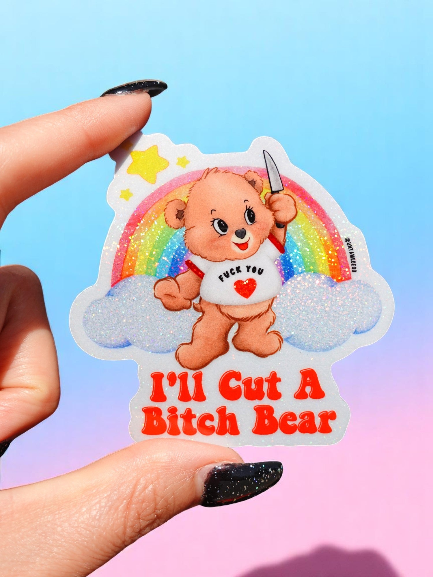 Sticker of a bear holding a knife with rainbow and cloud design, held by a hand against a colorful background.