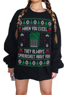 A person wearing a black crewneck sweatshirt with a green, white, and red Christmas-themed spreadsheet holiday graphic that reads 'WHEN YOU EXCEL THEY ALWAYS SPREADSHEET ABOUT YOU'.