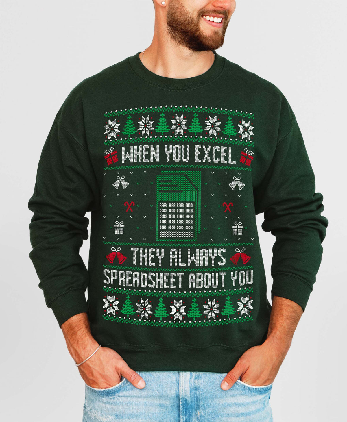 A man wearing a dark green crewneck sweatshirt with a festive holiday spreadsheet-themed graphic. The graphic features green and white snowflakes, Christmas trees, gift boxes, a spreadsheet icon, and the text 'WHEN YOU EXCEL THEY ALWAYS SPREADSHEET ABOUT YOU' in white.
