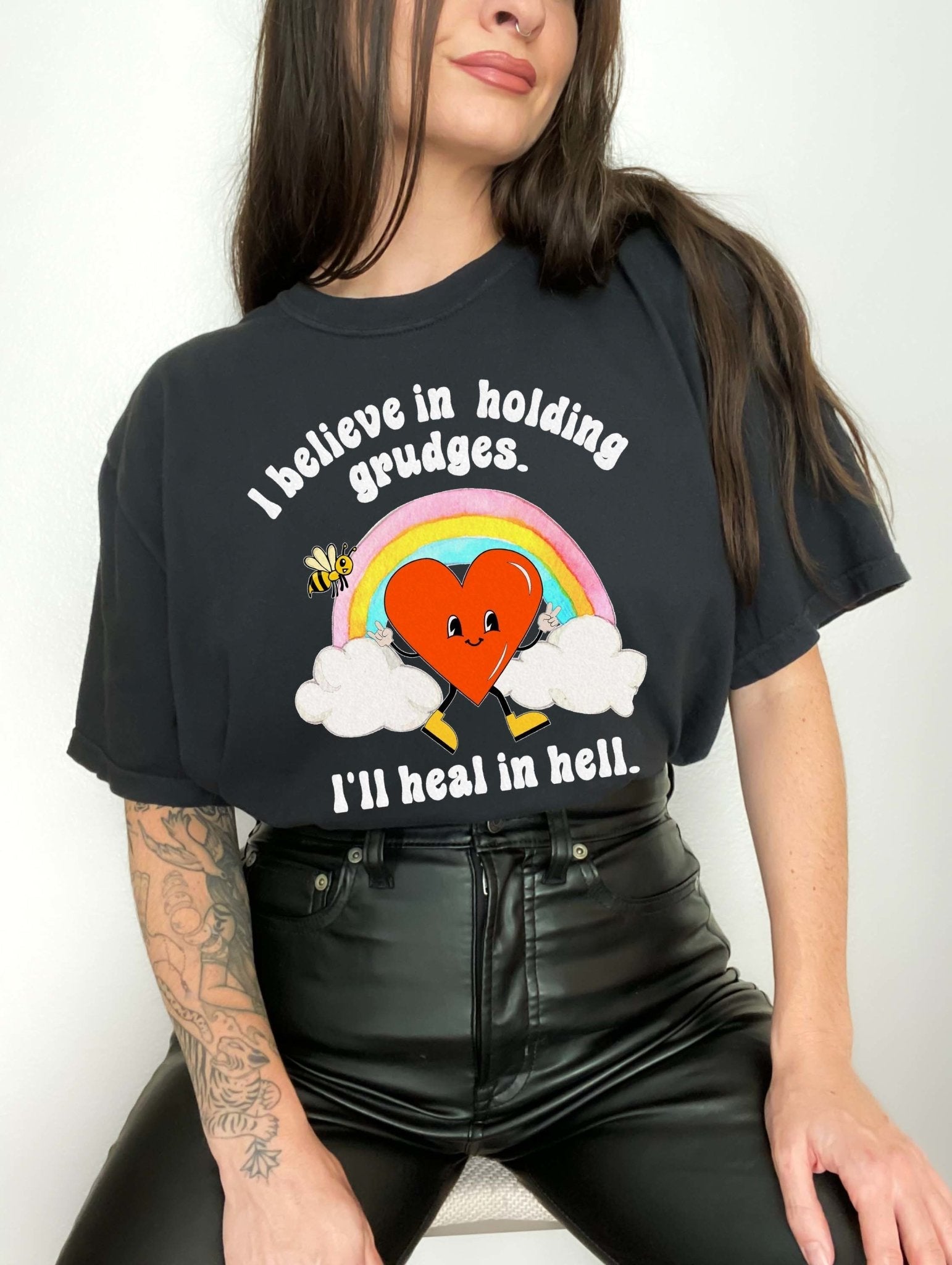 Funny sarcastic black t-shirt with retro heart and rainbow graphic reading I believe in holding grudges I’ll heal in hell