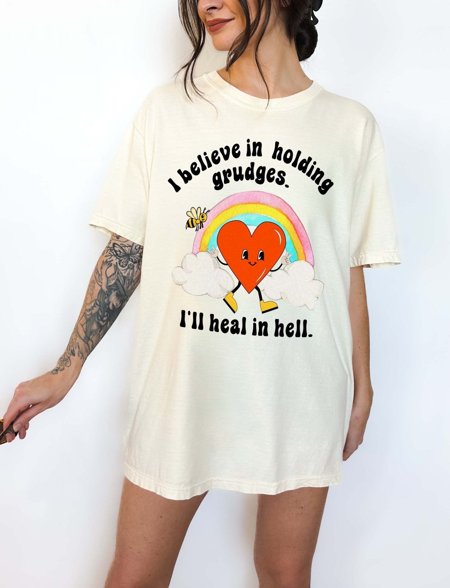 Funny sarcastic black t-shirt with retro heart and rainbow graphic reading I believe in holding grudges I’ll heal in hell